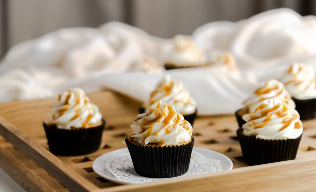 Cupcakes in black wrappers with white frosting and butterscotch drizzle on a serving tray. 
