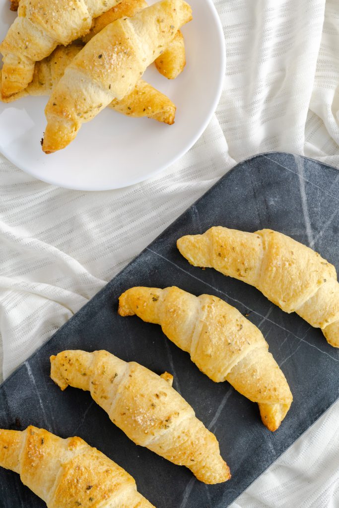Four garlic and cheese crescents on a dark marble serving board. 