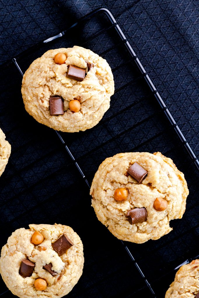 Brown butter chocolate chip cookies cooling on a black wire rack with a black background. 