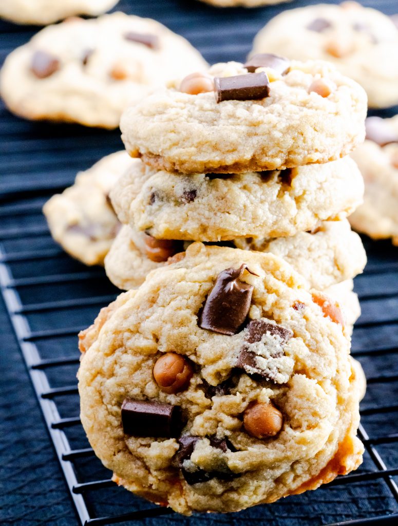 Stacked brown butter chocolate chip caramel cookies on a wire rack with cookies behind the stack. 