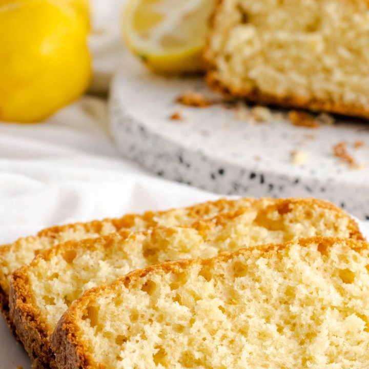 Freshly baked lemon bread in the background with slices on a plate in front.