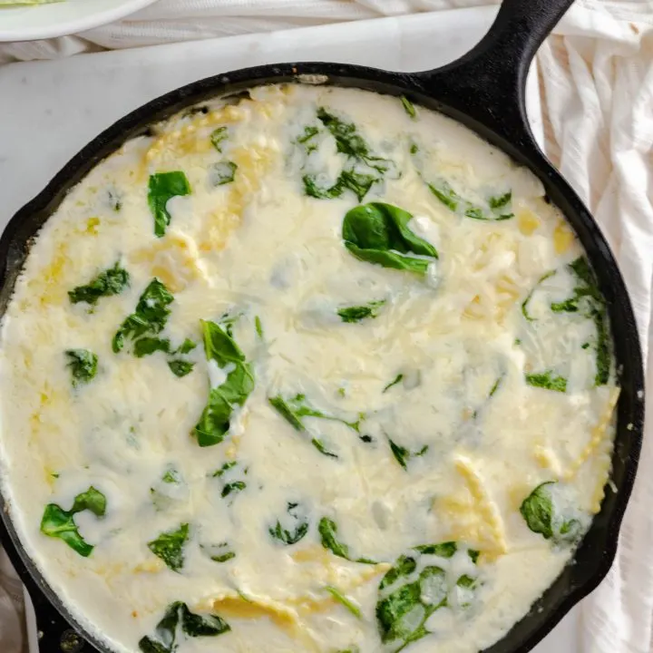 A large cast iron skillet with cheesy ravioli and chopped spinach.