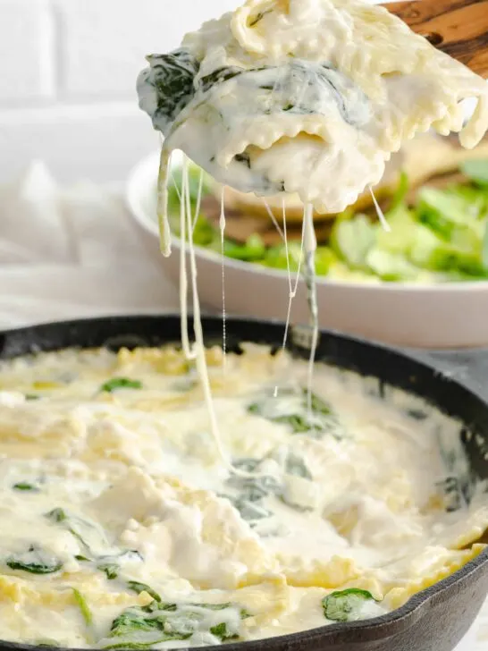 A serving spoon with cheesy spinach ravioli skillet.
