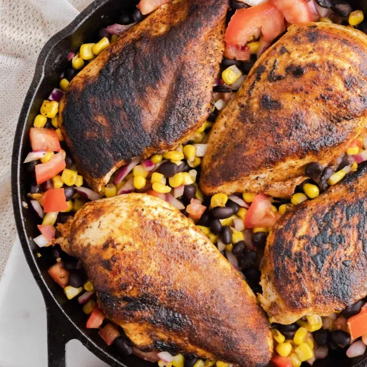 A cast iron skillet with bean salsa and blackened chicken.