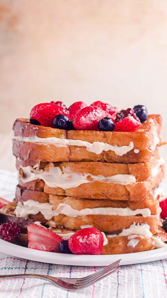 8 slices of cream cheese stuffed French toast on a white plate with fresh berries. 
