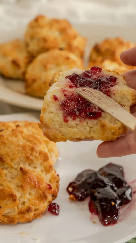 A drop biscuit split open with grape jelly being spread on it.