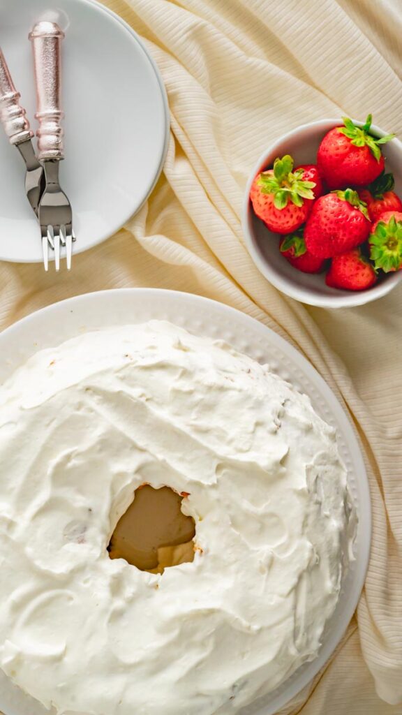 Whipped cream frosted angel food cake with a bowl of strawberries.