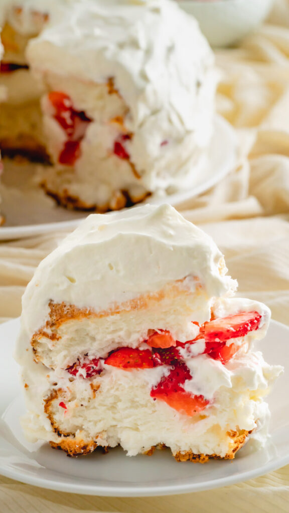 A slice of layered angel food cake with homemade whipped cream and fresh strawberries.