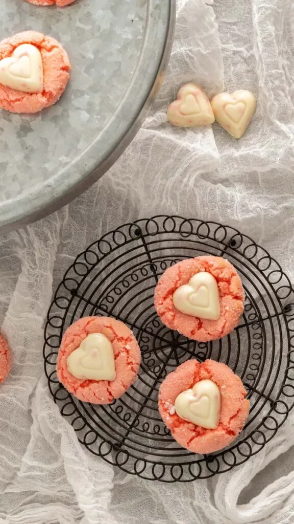 Three Valentine's Day cookies on a round decorative cooling rack with a linen background.