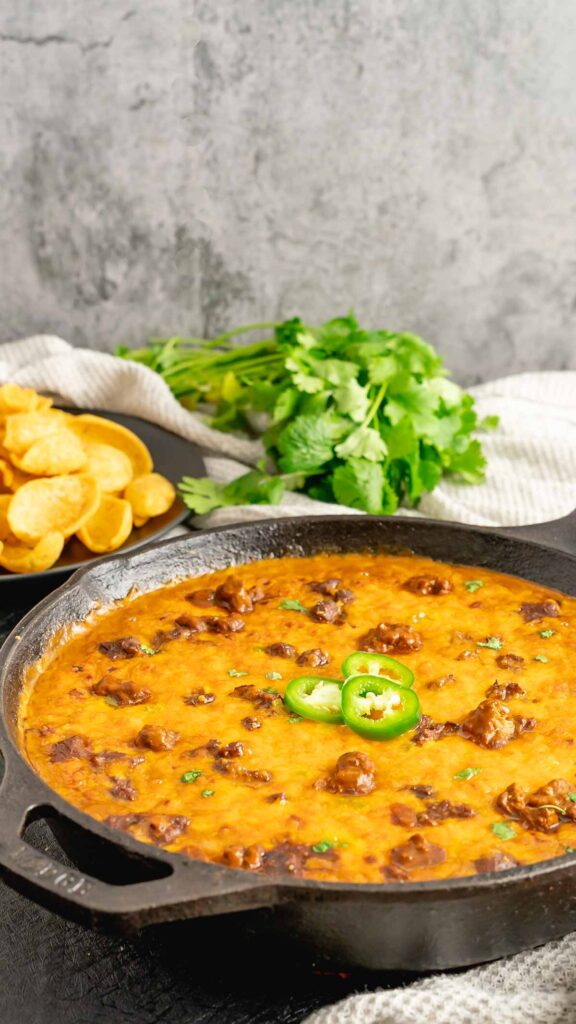 Sliced jalapenos served on broiled chili cheese dip with a dish of Frito scoops.