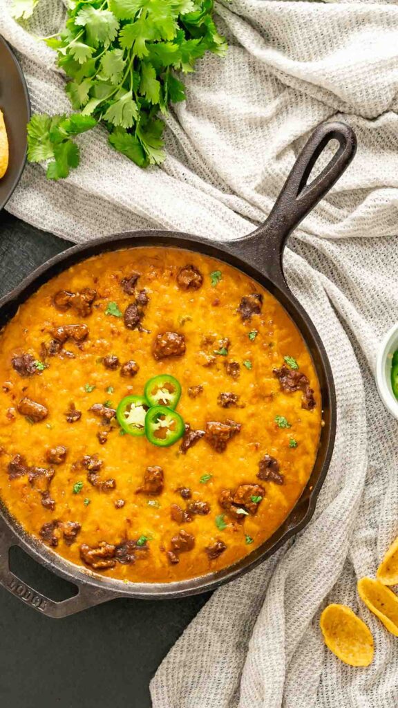 A cast iron skillet with chili cheese dip made in the Instant Pot and broiled in the oven.