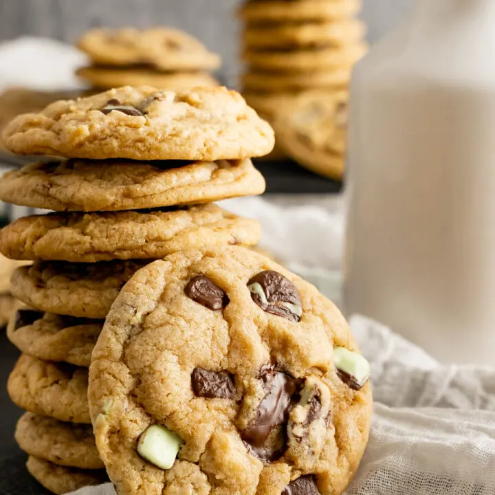 Chewy mint chocolate cookie propped against a stack of cookies with a cookie in the foreground.