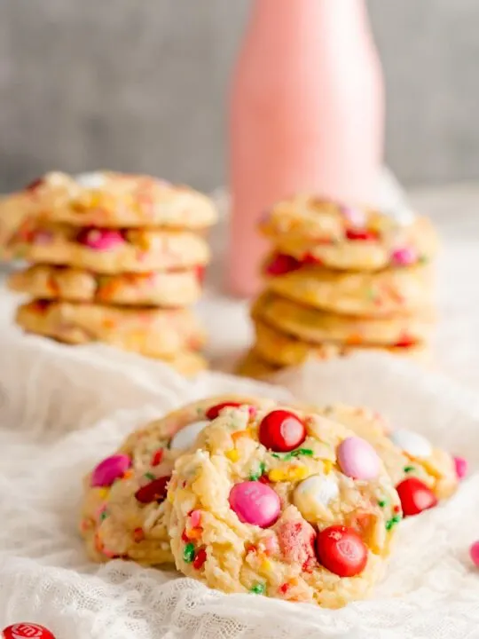 Funfetti cookies stacked in the background with strawberry milk and cookies up close.