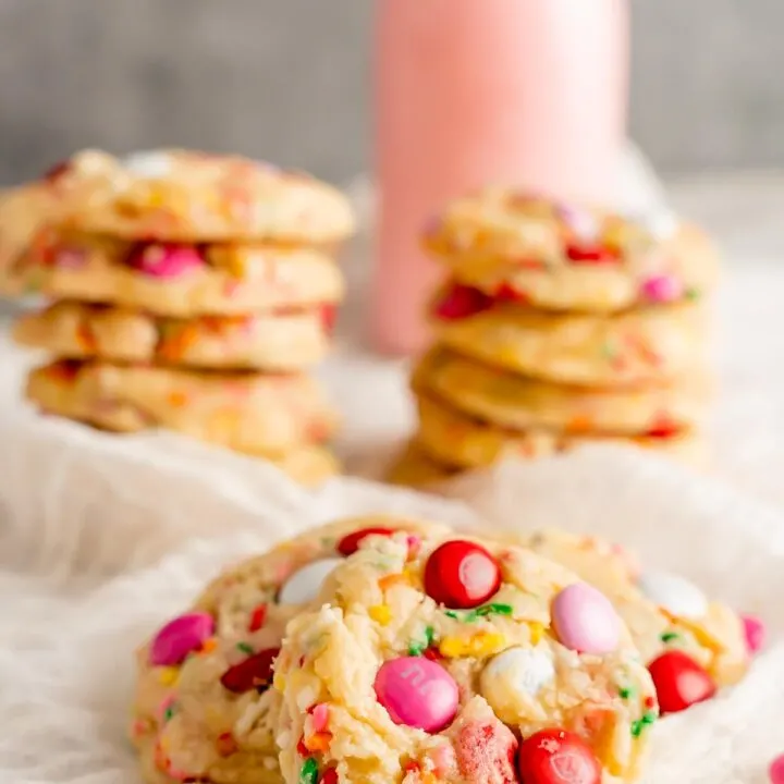 Funfetti cookies stacked in the background with strawberry milk and cookies up close.