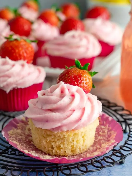 A strawberry lemon cupcake with the wrapper peeled with a strawberry to top.