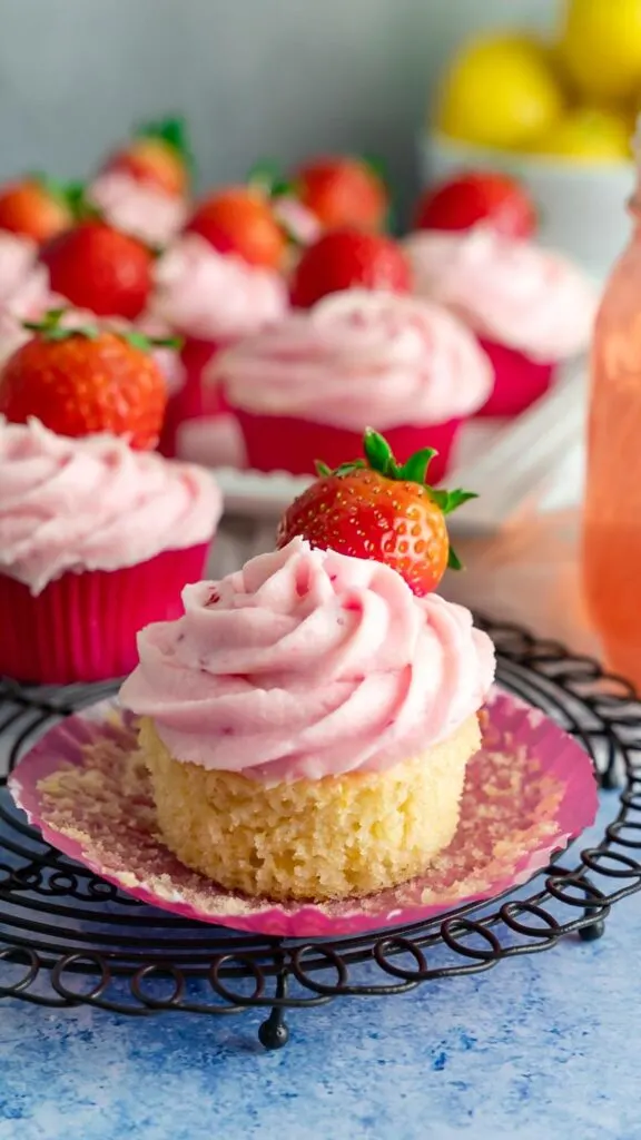 A strawberry lemon cupcake with the wrapper peeled with a strawberry to top.