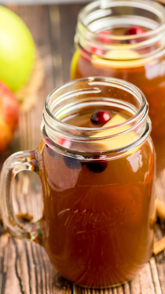 A jar of crockpot apple cider with fresh fruit.