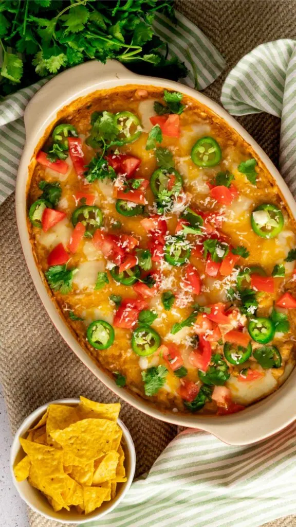 Birds eye view of hot taco dip with tomato, jalapeno, and cilantro toppings.